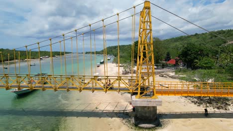 arial parallel of two tourists driving scooters across yellow suspension bridge in nusa ceningan and nusa lembongan island in bali indonesia