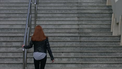 a beautiful young red-haired woman climbs the great concrete city stairs