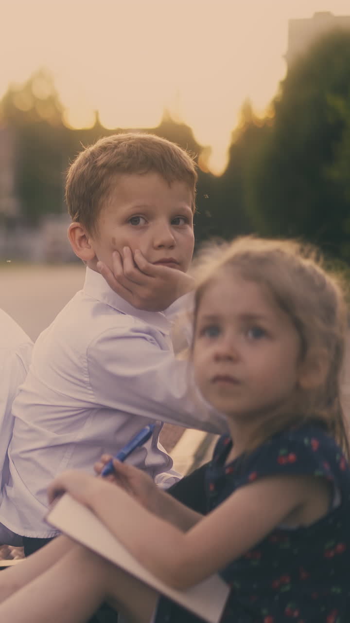 stressed schoolboy tired of preparing for test sits with friend and small sister on clean roadside against blurred house