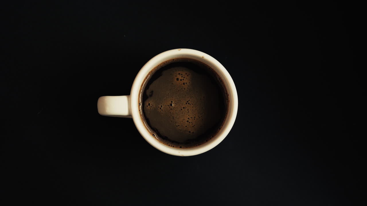 Minimal top-down shot of a black coffee mug on a dark background. Clean, modern composition with copy space, ideal for backgrounds, branding, lifestyle visuals, caffeine concepts, and text overlays