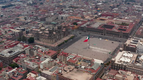 Erhöhter-Fliegender-Blick-Auf-Die-Catedral-Metropolitana-De-La-Ciudad-De-Mexico-Und-Die-Plaza-De-La-Constitucion-Mit-Riesiger-Staatsflagge.-Drohnenaufnahmen-Des-Historischen-Stadtzentrums.-Mexiko-Stadt,-Mexiko.