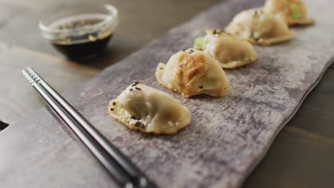 composition of plate with gyoza dumplings and soy sauce with chopsticks on wooden background