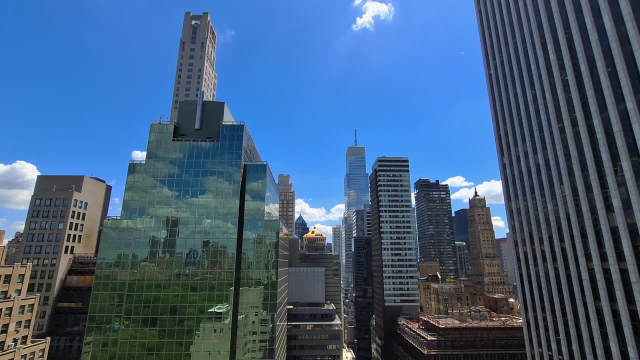 High-rise buildings with glass facades reflect sunlight and greenery from Central Park, viewed from above in Midtown Manhattan, New York, United States