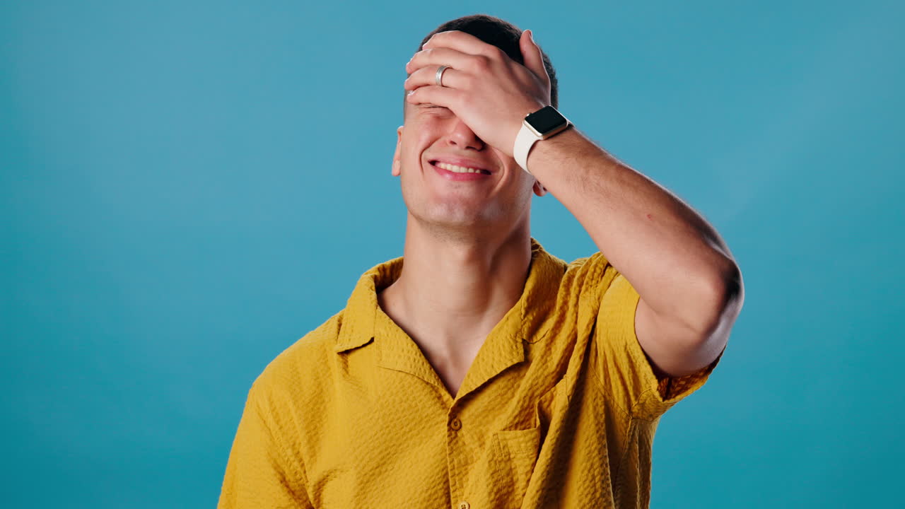 Man in yellow shirt laughing with hand on face