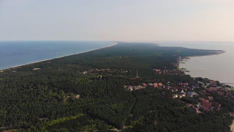 antena: volando hacia atrás y revelando un pequeño pueblo de pescadores cerca de la orilla del mar en el borde del bosque de pinos verdes