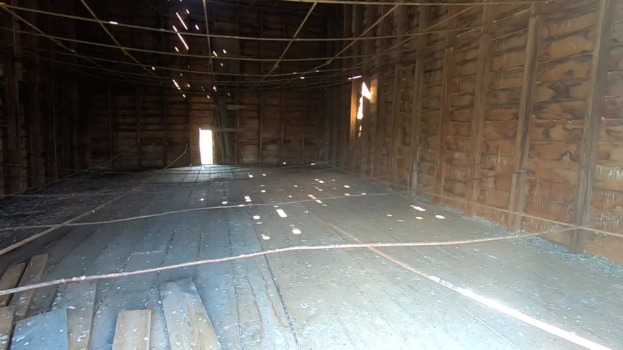 Inside a old dirty abandoned barn with beams hanging from the walls with light traveling through small openings in the roof.
