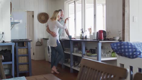 Happy-caucasian-mature-couple-drinking-coffee-and-looking-through-the-window-in-the-kitchen