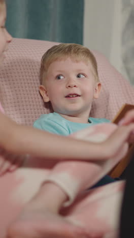 little boy examines book while mom and sister holding hands. happy family enjoys time together. woman sits in wheelchair interacting with kids closeup