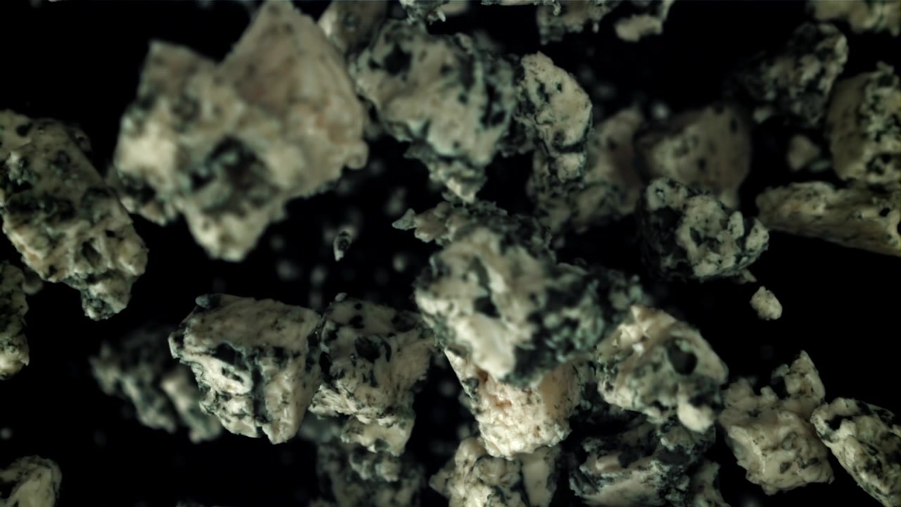 Blåskimmeloststykker faldende i super slowmotion på sort baggrund