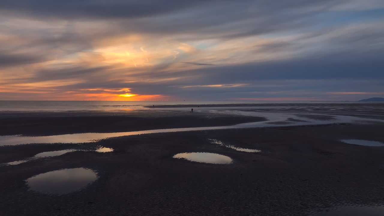 Flying over tidal pools towards fisherman and setting sun. Fleetwood, Lancashire, UK.