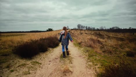 Blond-child-running-up-path-in-winter-sand-dune-landscape-slow-motion