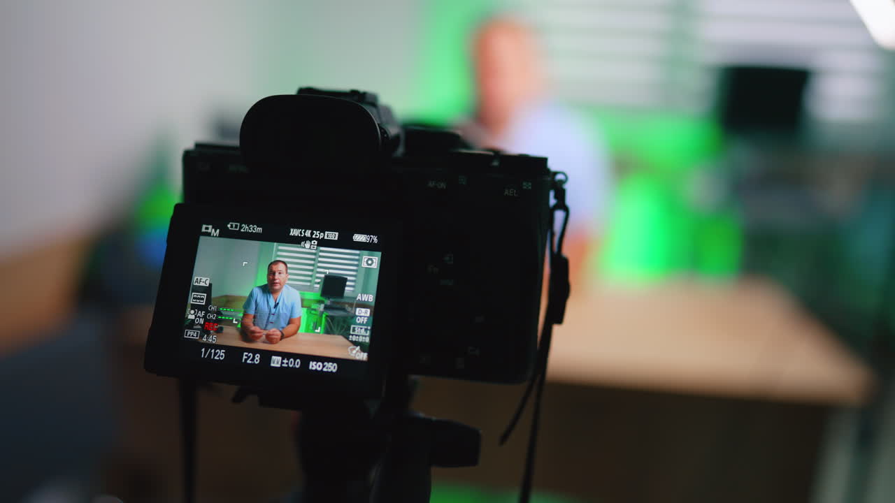 Schermo della Fotocamera Mostra Medico che Registra Vlog Medico. L'LCD della fotocamera mostra un medico in camice blu durante la registrazione di un vlog clinico con retroilluminazione verde.