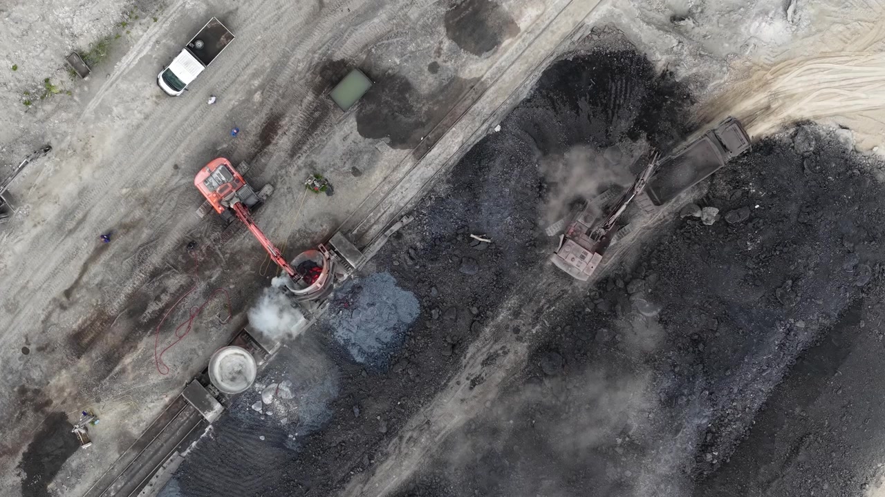 An aerial drone view captures excavators working in a large coal mine, loading raw material for energy production, showcasing industrial operations.