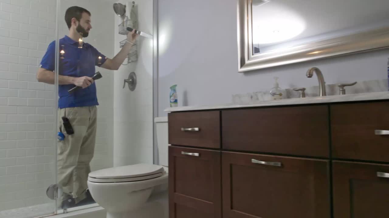 Home Inspector stands in a glass shower enclosure checking for leaks in the caulking seal
