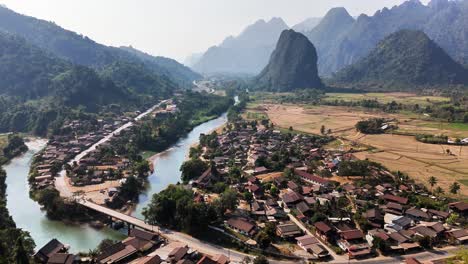 aerial orbit of pha tang village nestled between limestone karst peaks, lush farmland, and the nam song river near vang vieng in laos, showing the scenic rural valley from above