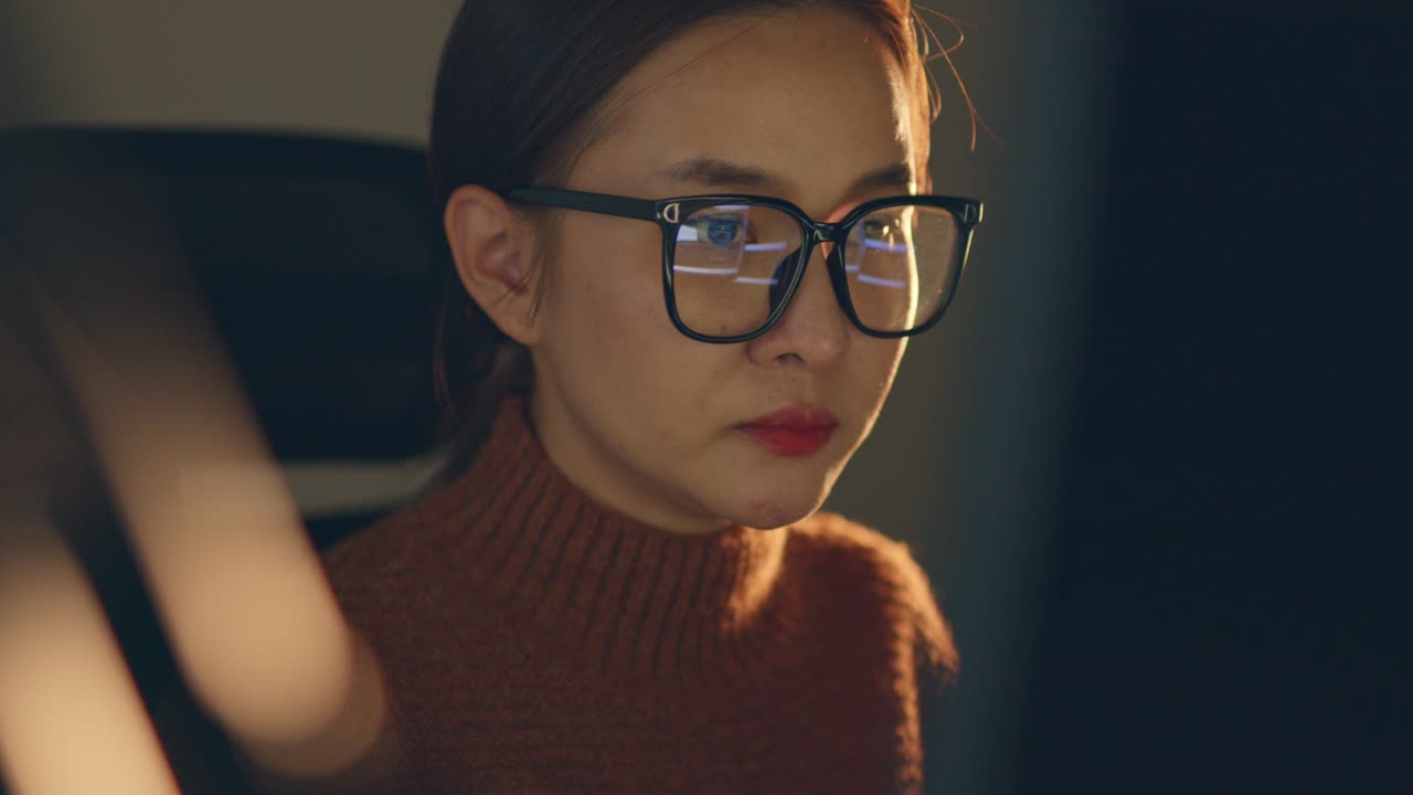 Young Asian woman, developer programmer, software engineer, IT support, wearing glasses working hard at night overtime on computer to check coding in bugging system.