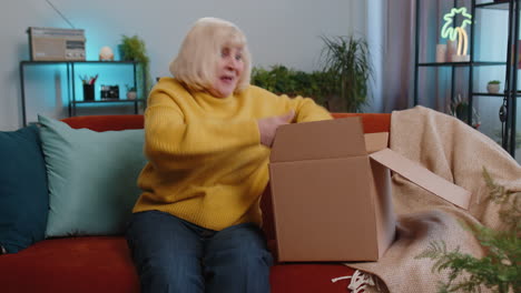 Grandmother-woman-shopper-unpacking-cardboard-box-delivery-parcel-online-shopping-purchase-at-home