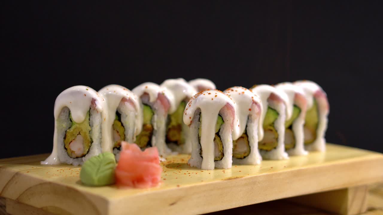 rollo de sushi con salsa encima espolvoreado con coberturas rojas, servido en un plato japonés de madera