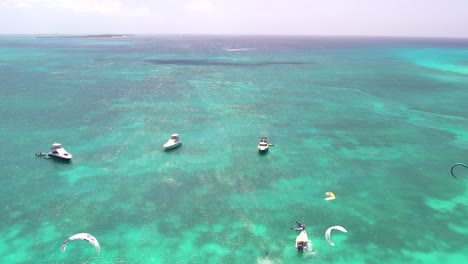 aerial shot caribbean beach people kitesurf near coast on turquoise sea water, tilt up