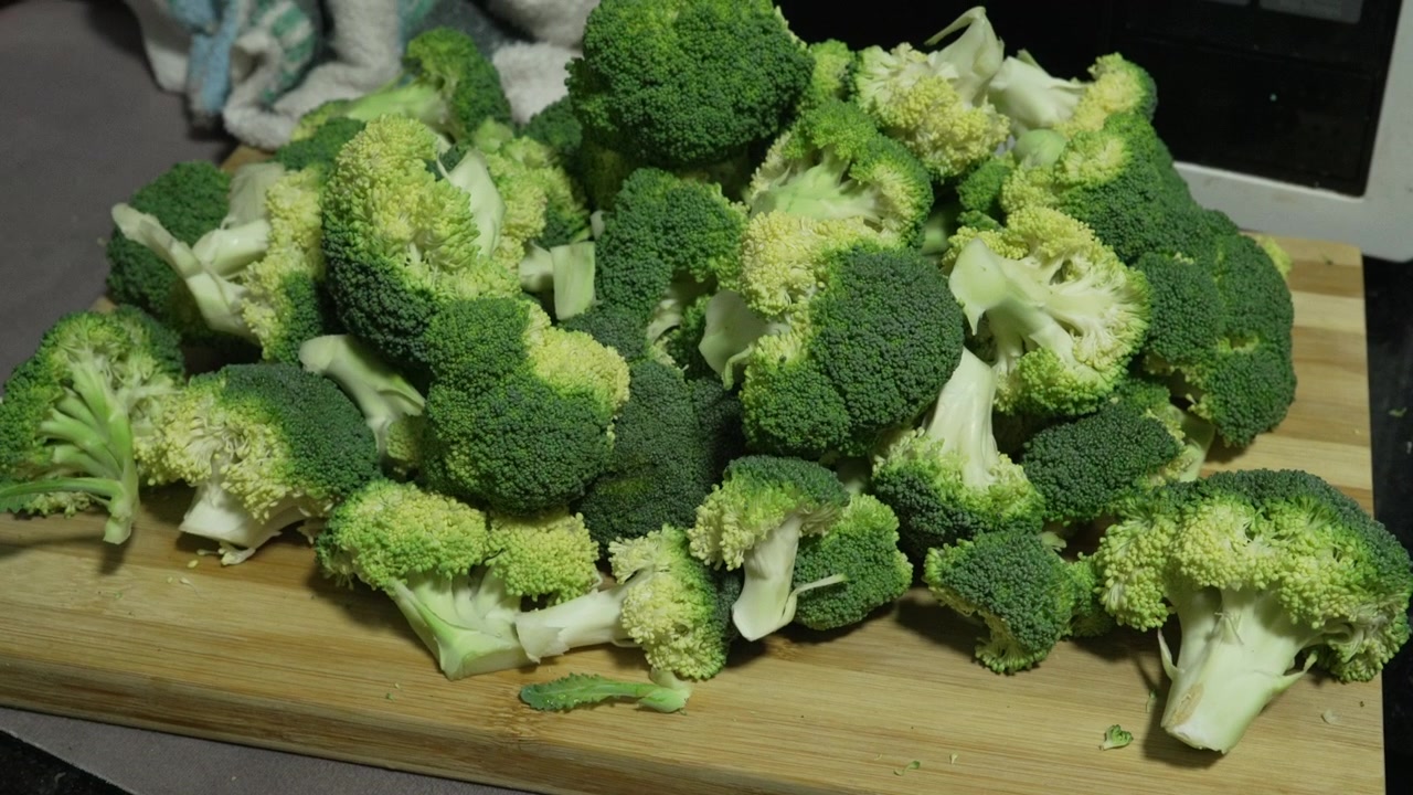 Cimette di broccoli tagliate formano un grande mucchio su un tagliere di legno in una cucina domestica, una semplice preparazione per pasti sani o video di ricette