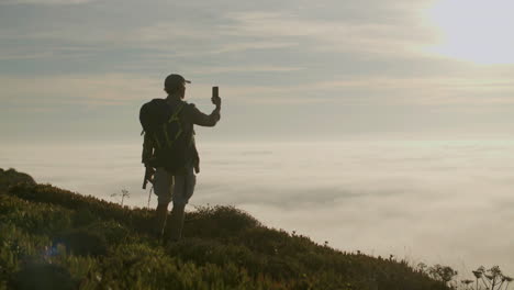 älterer wanderer, der auf dem berg steht und die schöne aussicht fotografiert