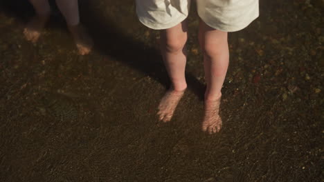 children stand barefoot in water on dark sand in tourist area. comfortable water temperature for relaxation on sunny day. spending leisure time together