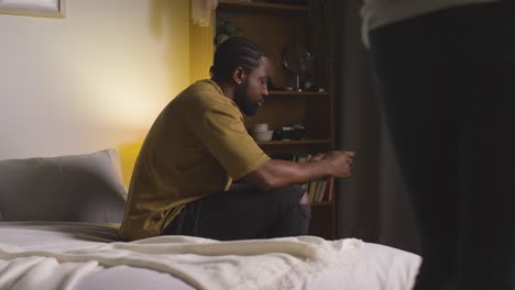 young couple relaxing at home at night with man scrolling internet on mobile phone talking to woman