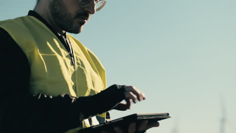 Um-Nachhaltige-Energie-Voranzutreiben,-überprüft-Ein-Professioneller-Ingenieur-Mit-Weißem-Helm-Und-Reflektierender-Weste-An-Einem-Sonnigen-Tag-In-Einem-Feld-Sauberer-Energieerzeuger-Mit-Einem-Tablet-Windkraftanlagen