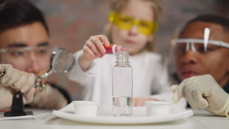 little girl drips red paint into bottle at teachers control