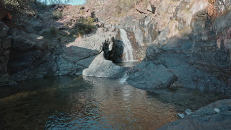 cascada serena en un terreno rocoso con aguas claras que reflejan el ambiente tranquilo de la naturaleza, toma amplia