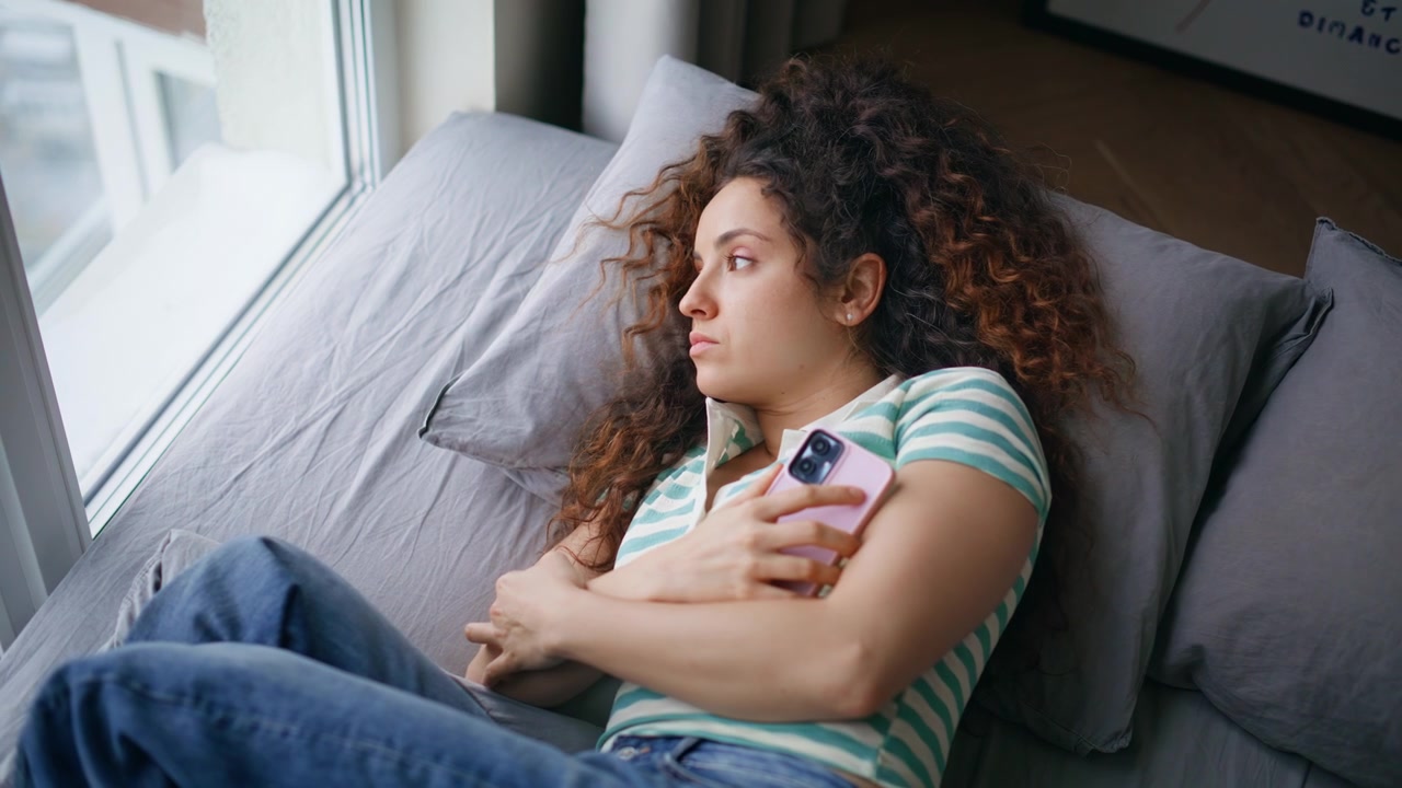 Donna sdraiata sul divano che scorre il telefono. Giovane donna pensierosa che fantastica sul weekend a casa.