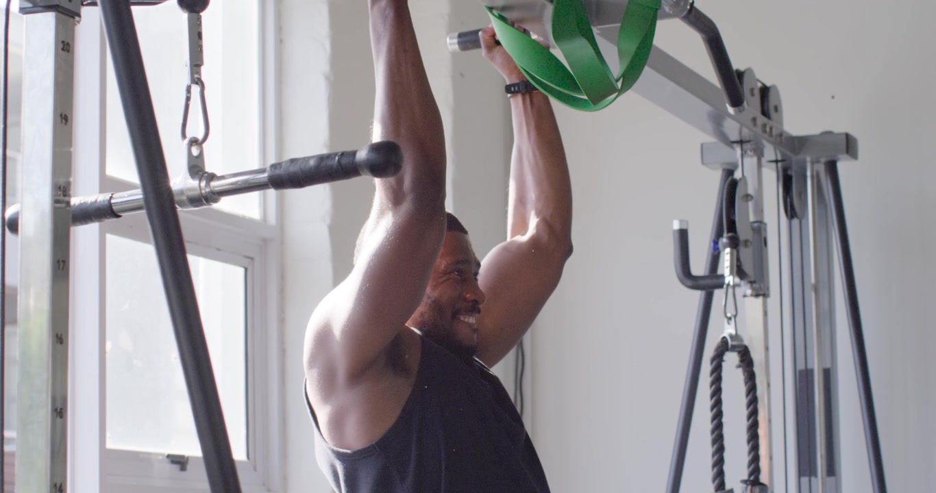 Man doing pull-ups with green band looped over bar at gym, wearing tank for strength