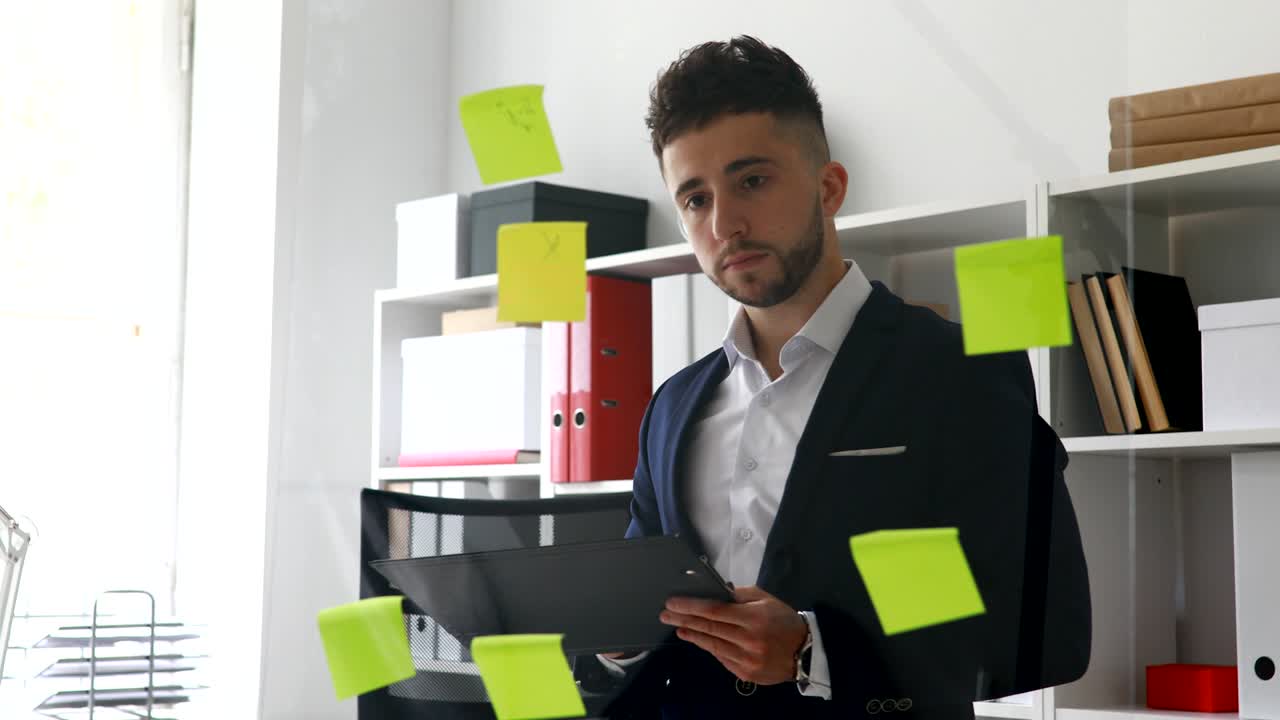 uomo d'affari in abito che fa appunti in documenti in piedi vicino al muro di vetro