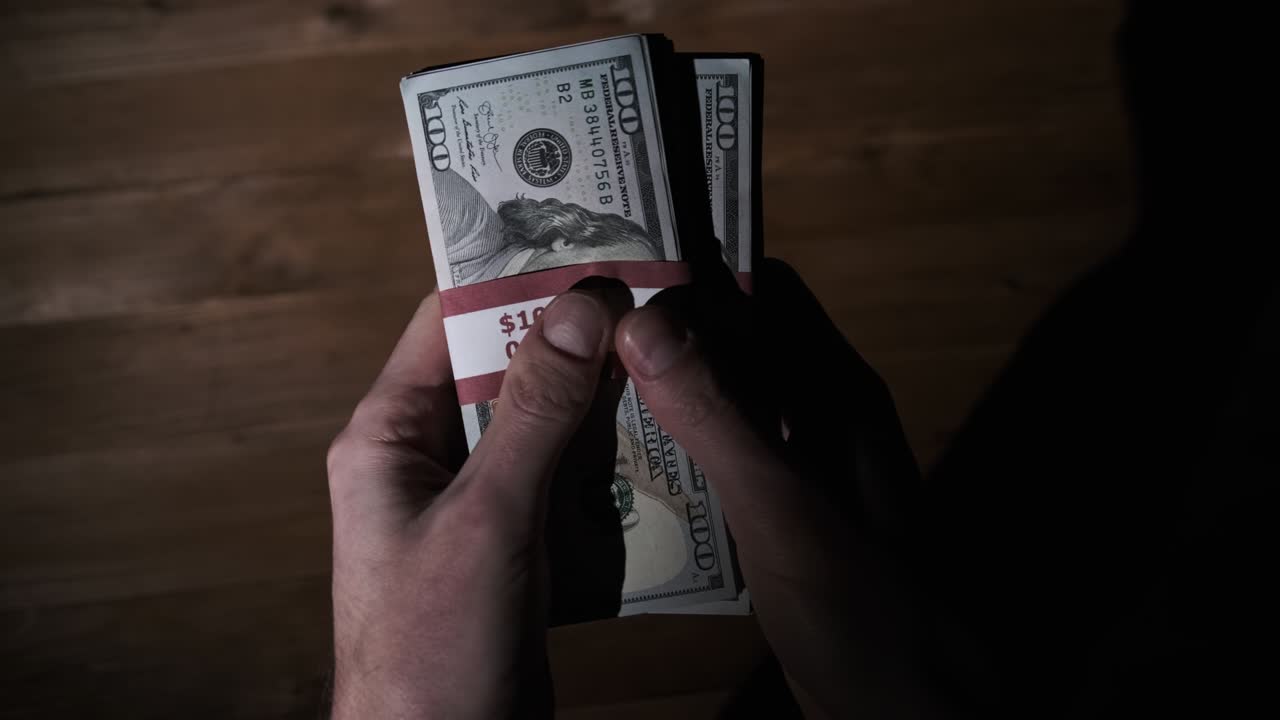 Male Hands Hold Three Stacks of 10000 US Dollar Bills on Wooden Background