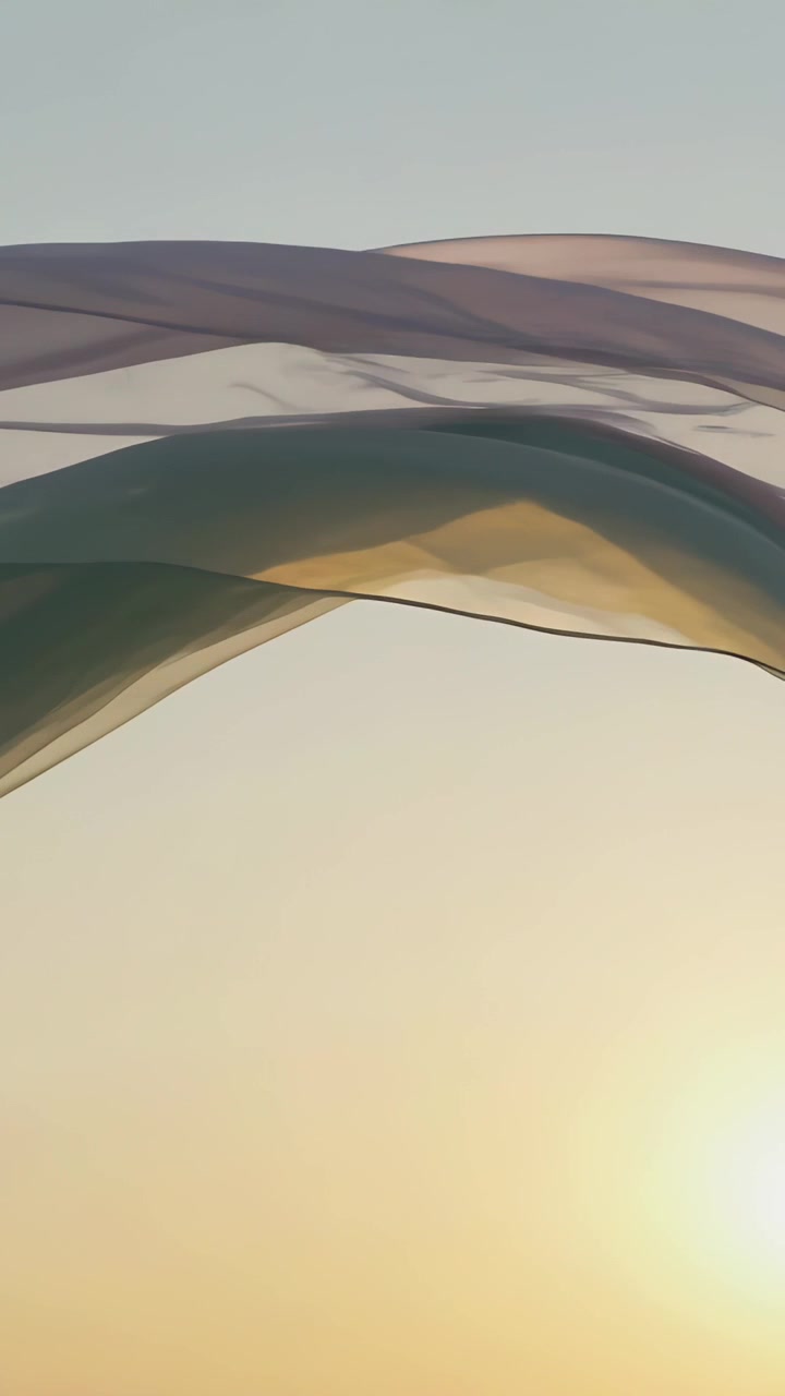 Vertical video: Light breeze sending sheer chiffon fabric arching across sunset sky, backlit sun