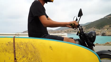 young man drives motorcycle with yellow surfboard attached looking for ideal spot for water kitesurfing