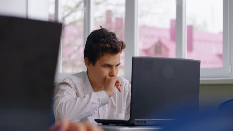 un adolescente estudiando en una computadora portátil en un aula
