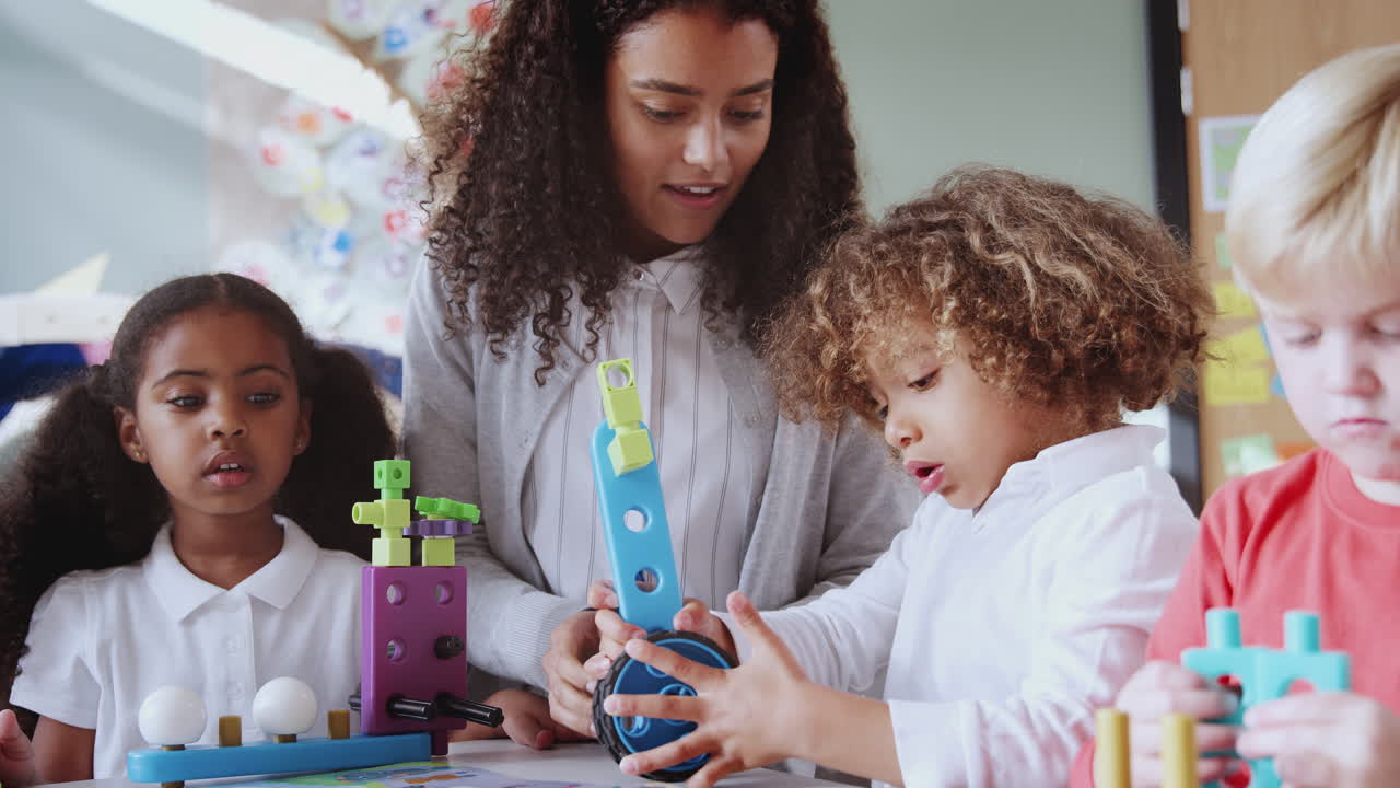 Female infant school teacher at table with three children using constructing blocks, selective focus