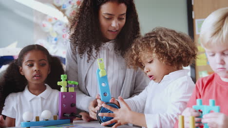 Female-infant-school-teacher-at-table-with-three-children-using-constructing-blocks,-selective-focus