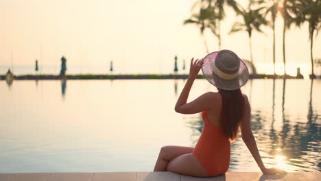 Golden-hour-sunlight-and-pretty-sexy-asian-woman-sitting-on-pool-border,-luxury-tropical-vacation-concept,-full-frame