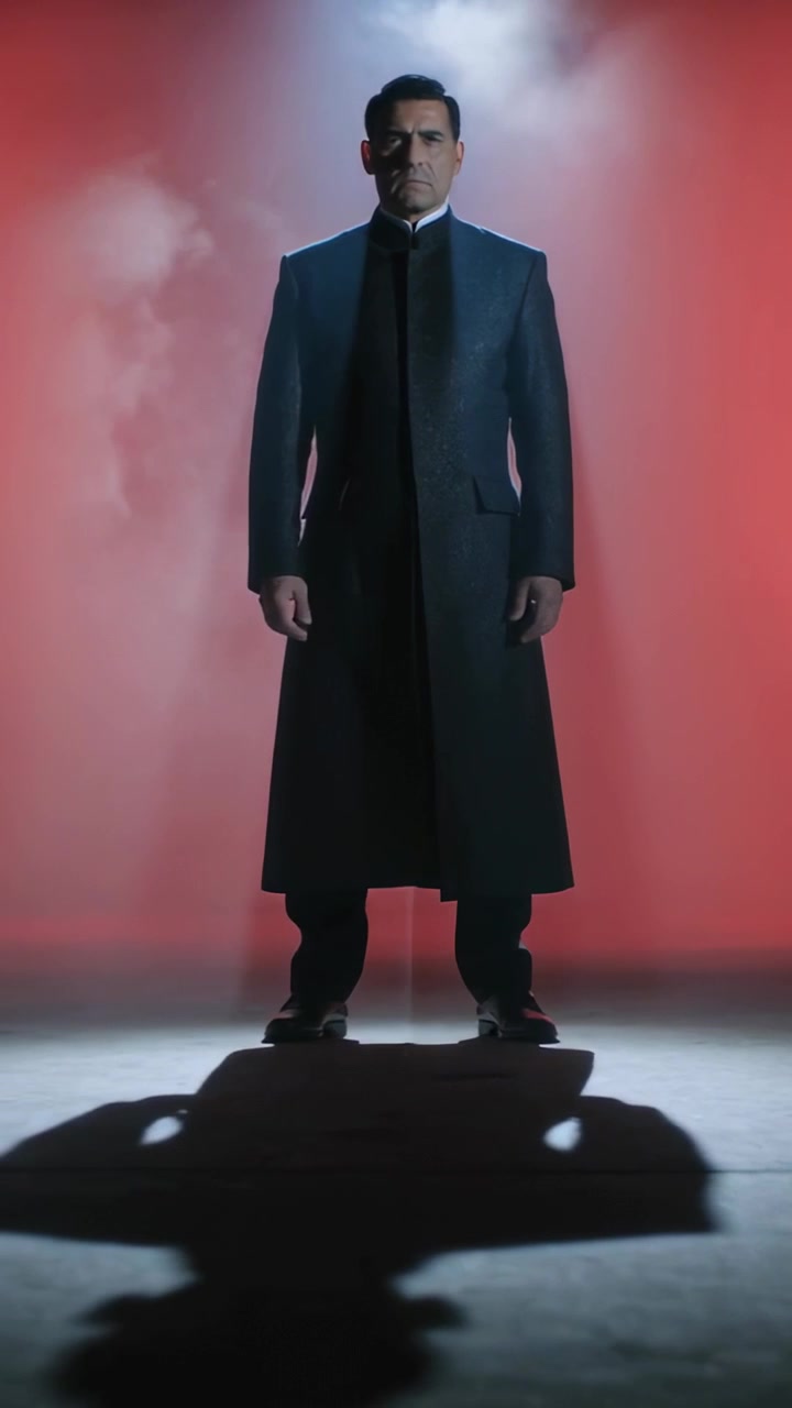 Video verticale: Un fascio di luce che colpisce un uomo in cappotto in piedi su un set rosso, con nebbia che si dirada per la rivelazione.