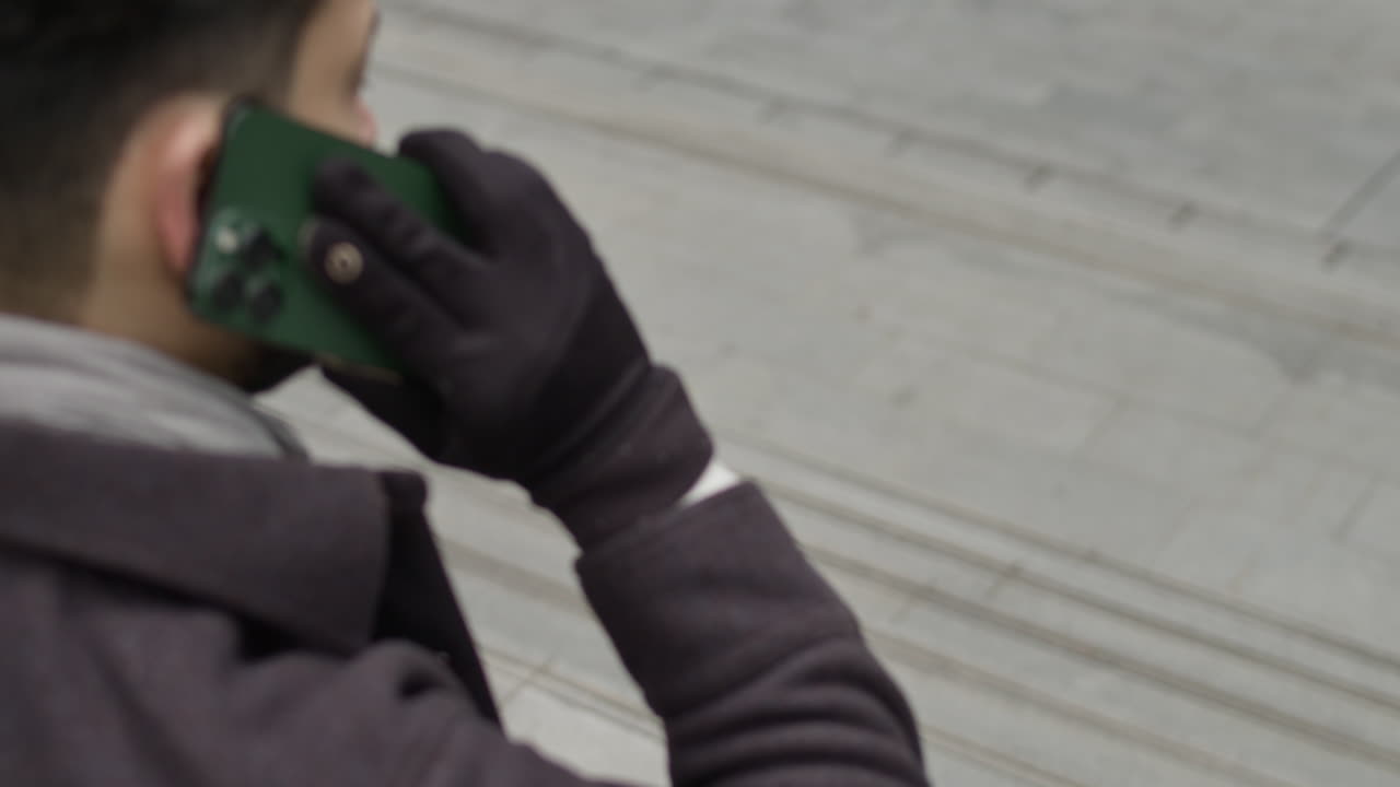 hombre en traje de otoño causal, se sienta en las escaleras de hormigón de un edificio de oficinas de negocios, habla activamente por teléfono