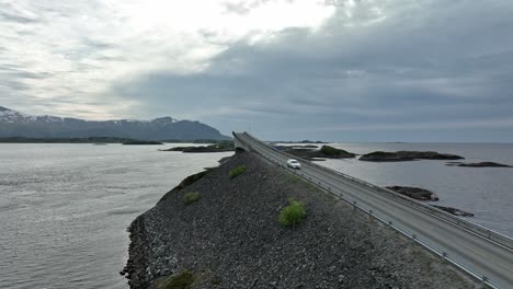 atlantic ocean road in norway - aerial passing over famous road while looking at iconic storseisundet bridge and north sea in background