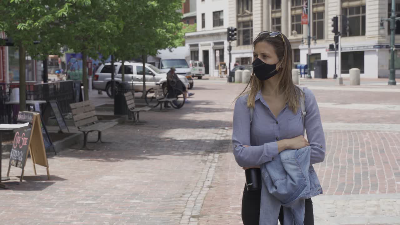 Chica caminando sola por la acera con mascarilla de protección negra durante la pandemia de coronavirus