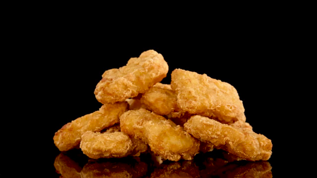 Golden, crispy chicken nuggets rotate in slow motion against a glossy black surface, highlighting texture and seasoning with dramatic studio lighting and smooth camera movement