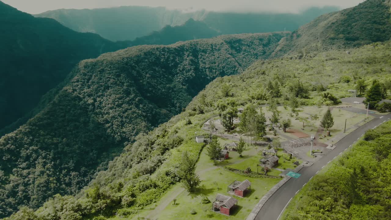 Ripresa aerea 4K di case sul bordo di un canyon verde intenso con alte montagne sullo sfondo.