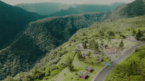 4k aerial houses on edge of deep green canyon with high mountains in background