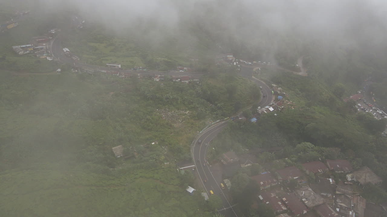Voertuigen die tussen huizen en groene begroeiing rijden op een mistige dag in Jakarta, Indonesië - drone-opname vanuit de lucht