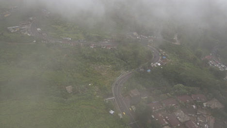 Vehicles-Passing-Between-Houses-And-Green-Vegetation-On-A-Misty-Day-In-Jakarta,-Indonesia---aerial-drone-shot