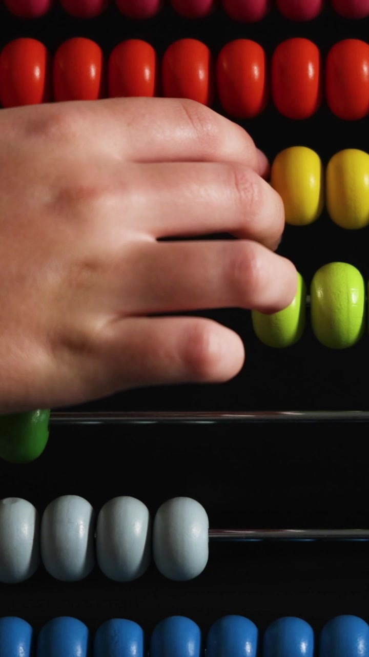 A vertical close-up shot showing a child's hand manipulating colorful beads on a traditional abacus.